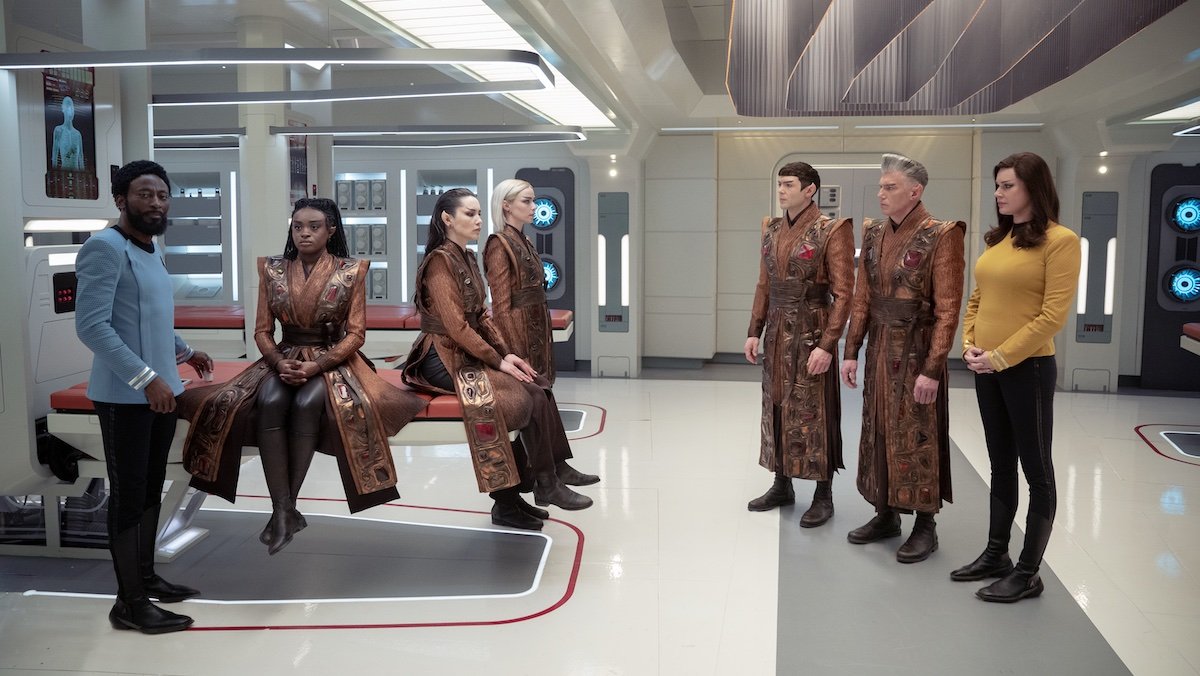 Characters, som in Starfleet uniforms other in tradtional Vulcan robes, in a brightly lit hospital bay on Star Trek: Strange New Worlds