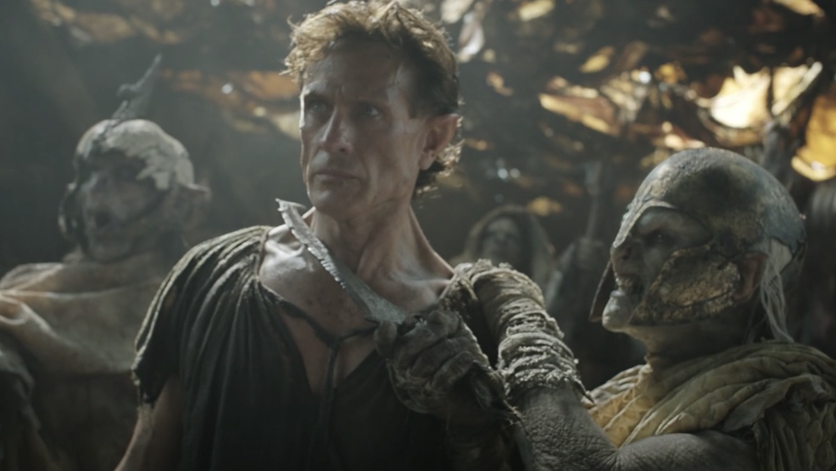 An orc holds a knife to an elf's throat on The Rings of Power, the Orcs are lead by Adar